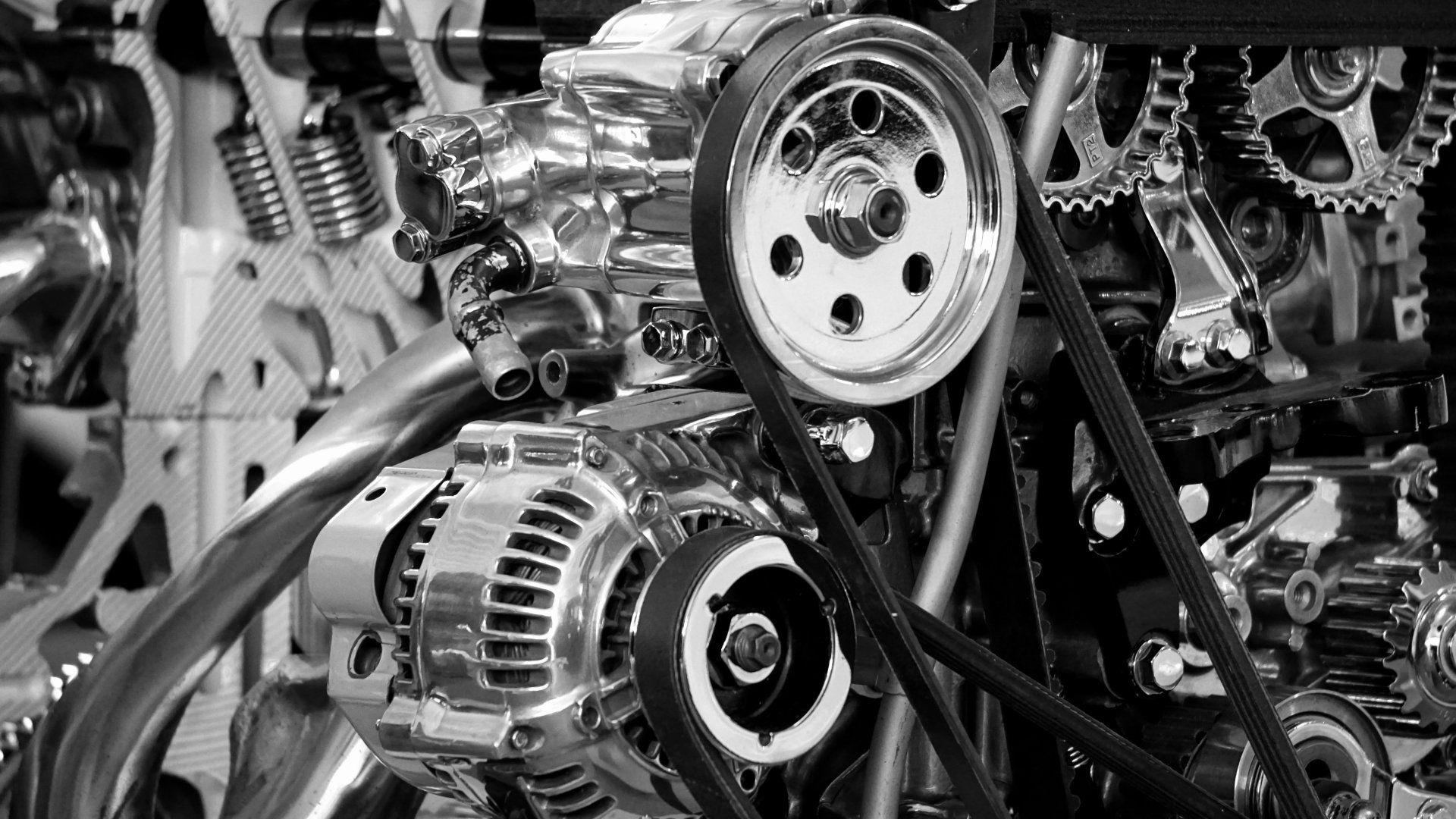 Close-up of car engine components with pulleys, belts, and metal gears in black and white