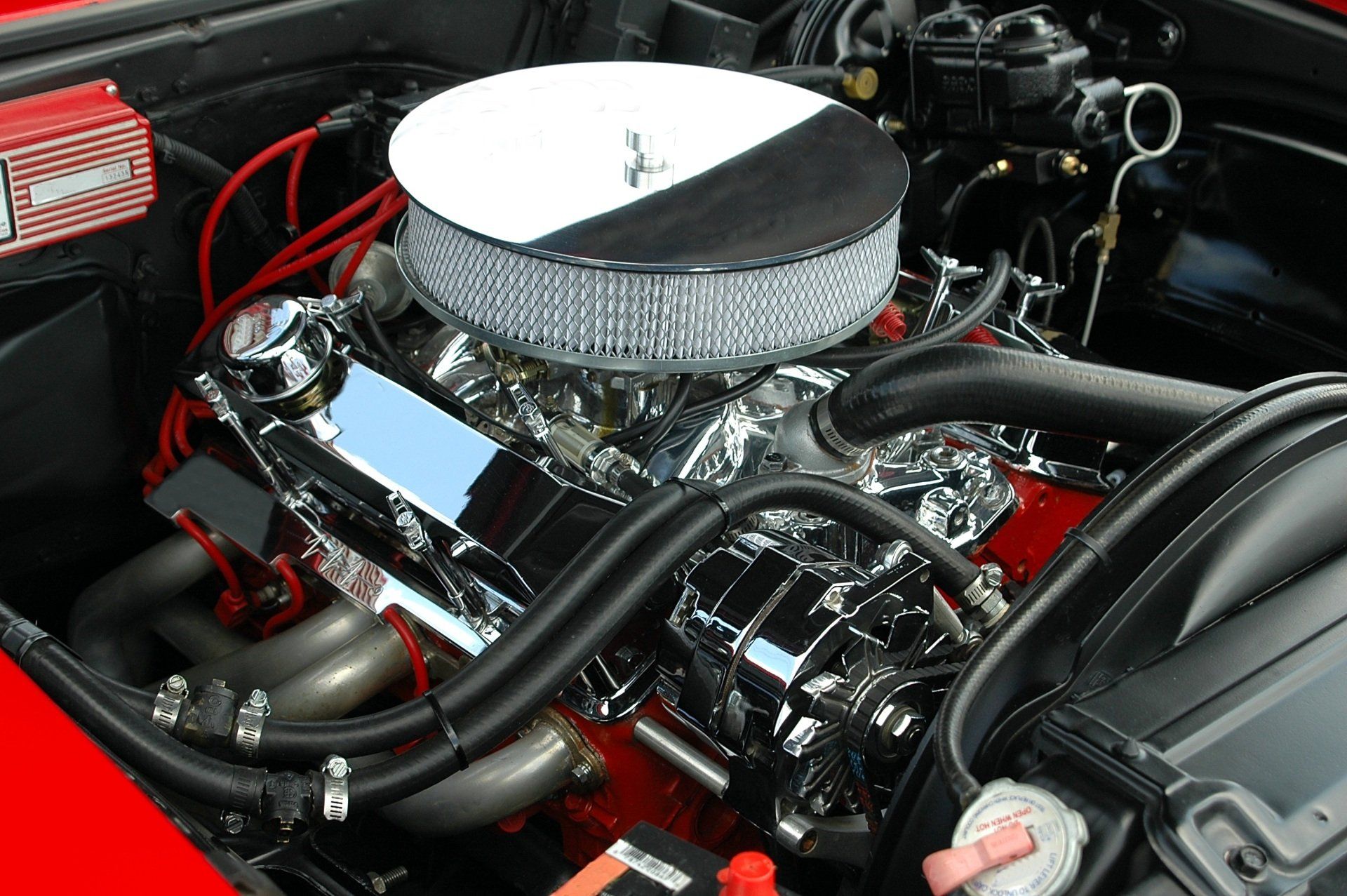 Shiny car engine with chrome parts, black hoses, and round air filter under the hood
